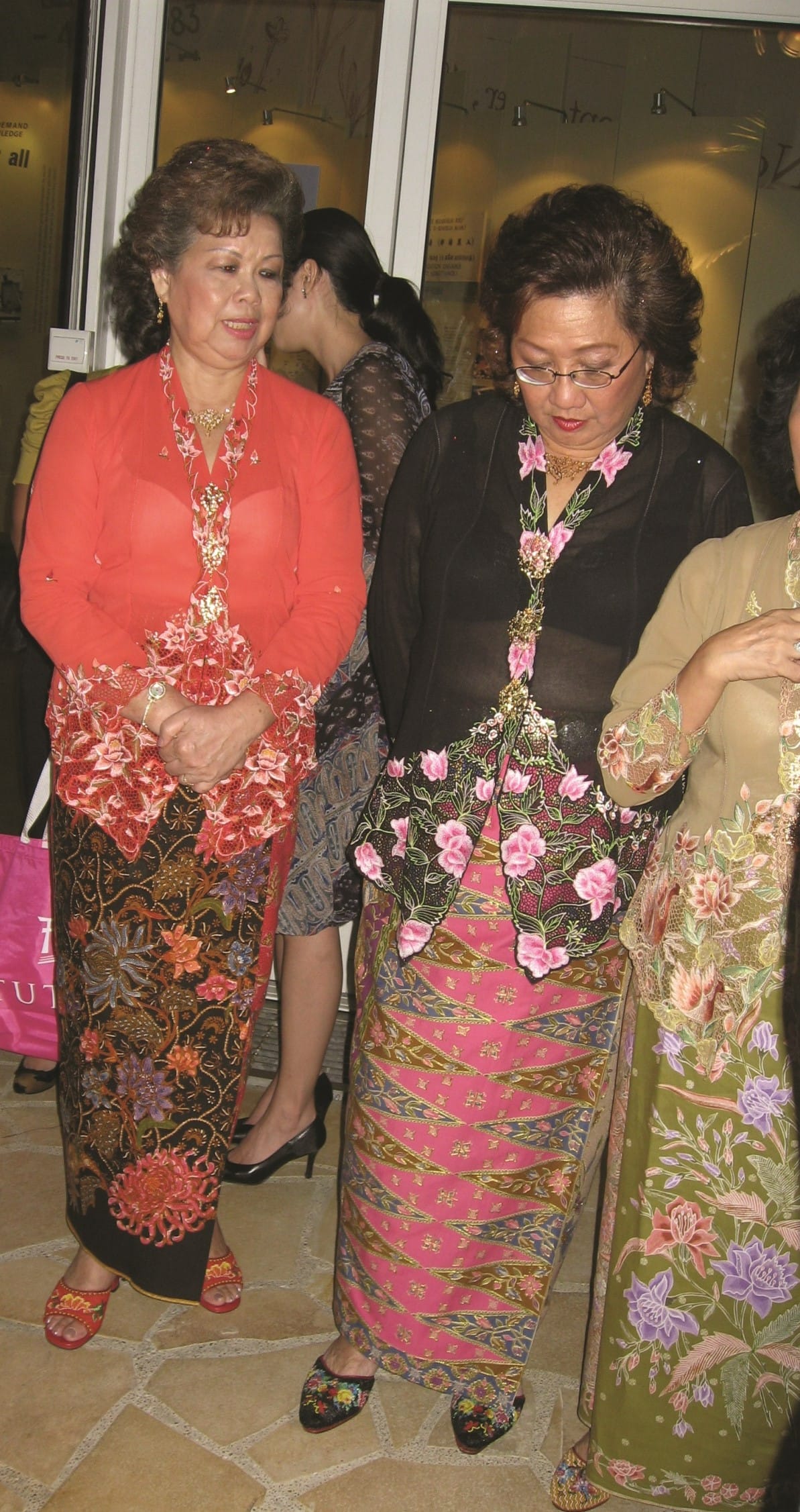 Four women are standing, showcasing colorful, floral traditional attire with intricate designs.